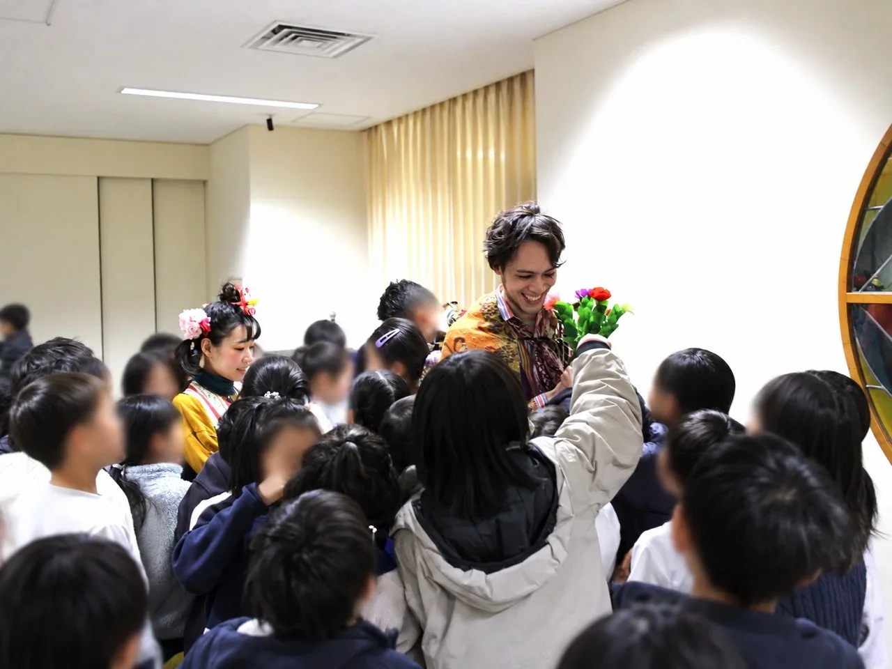 公演後、花を手にした役者を子どもたちが囲み、笑顔で交流する様子。